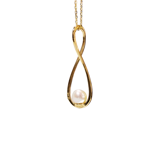 The infinity pendant has the 14k gold chain threaded through the top loop of the 14k gold infinity shape with a genuine pearl set to be cradled by the bottom of the infinity loop and is hanging against a pure white background in a way that the angle shows you the 14k stamp along the left leg of the design.