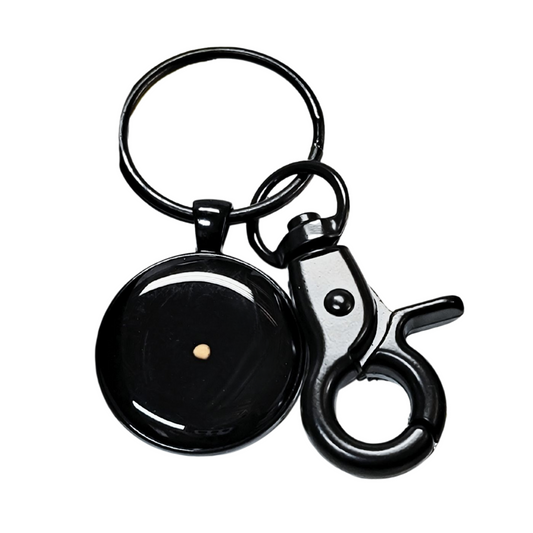 Close-up image of a large black keychain featuring a round pendant with a single real mustard seed sealed in clear resin at the center. The pendant is encased in a glossy black bezel, giving it a sleek and modern appearance. Attached to a sturdy key ring, the keychain also includes a black swivel trigger clasp for smooth, secure attachment to keys, bags, or gear. A meaningful, faith-based accessory with minimalist design.