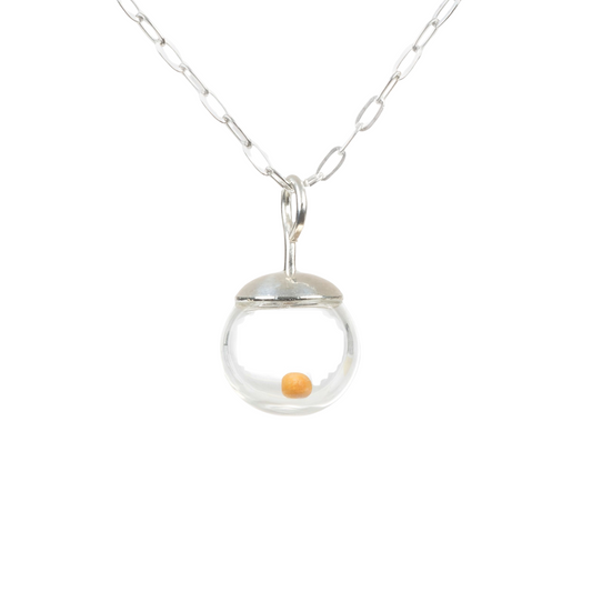 Close-up photo of a delicate 8mm mustard seed necklace (pendant is about 1/4 inch diameter)  featuring a tiny real mustard seed encased in a clear hand-blown glass globe. The globe is topped with a smooth, solid 925 sterling silver cap and suspended from a fine sterling silver cable chain. The mustard seed floats freely inside the miniature globe, creating a simple yet meaningful design.