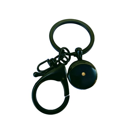 Black metal keychain with a round keyring, lobster clasp, and a small charm featuring a black bezel that holds a single mustard seed encased in clear resin.