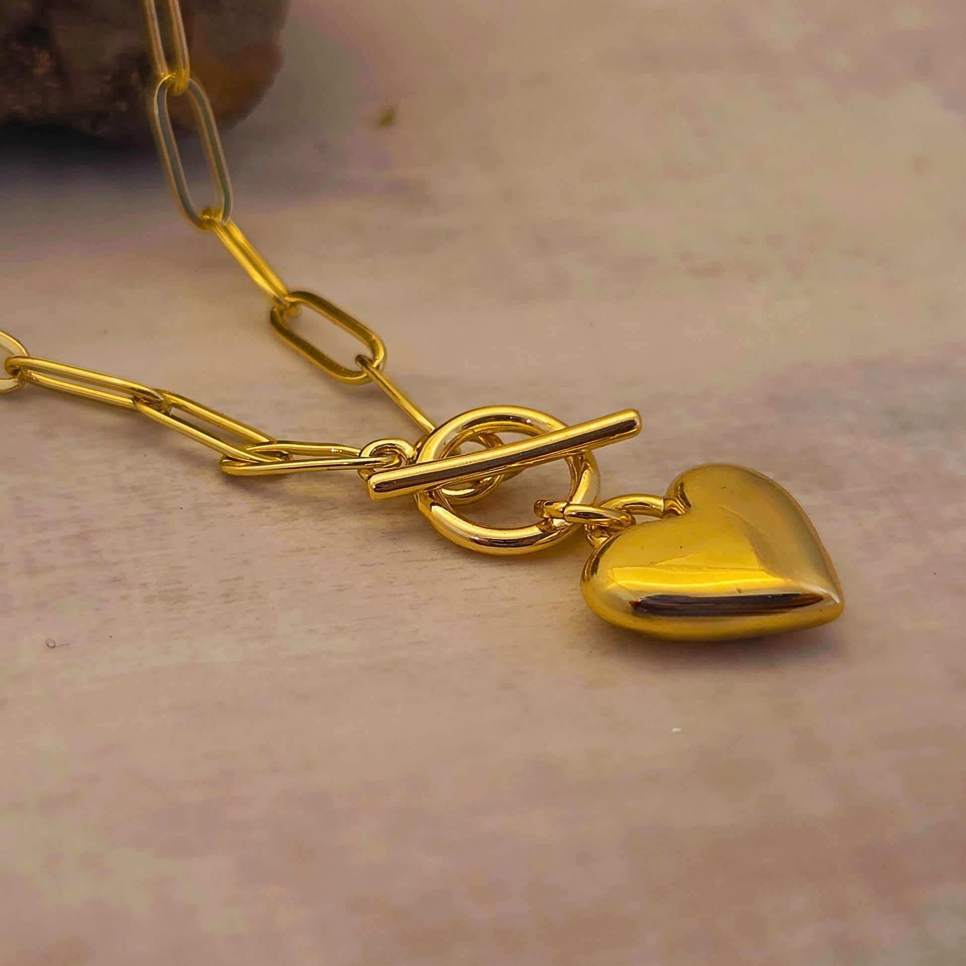 Gold heart-shaped pendant on a chain against a neutral background