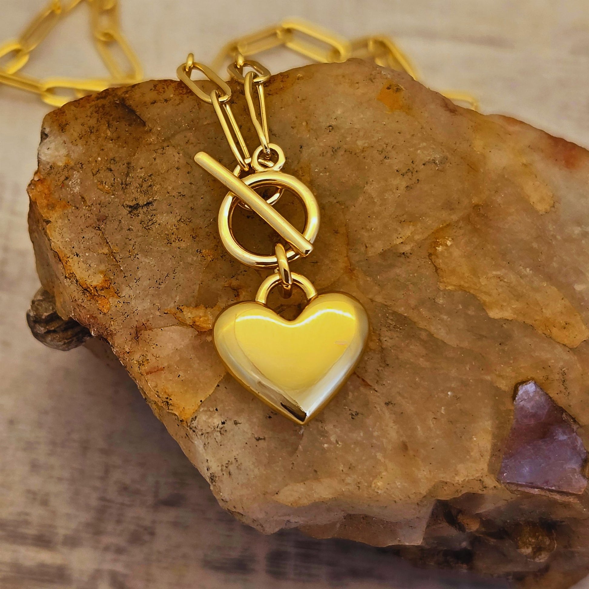 Gold heart-shaped pendant on a gold chain resting on a rock.