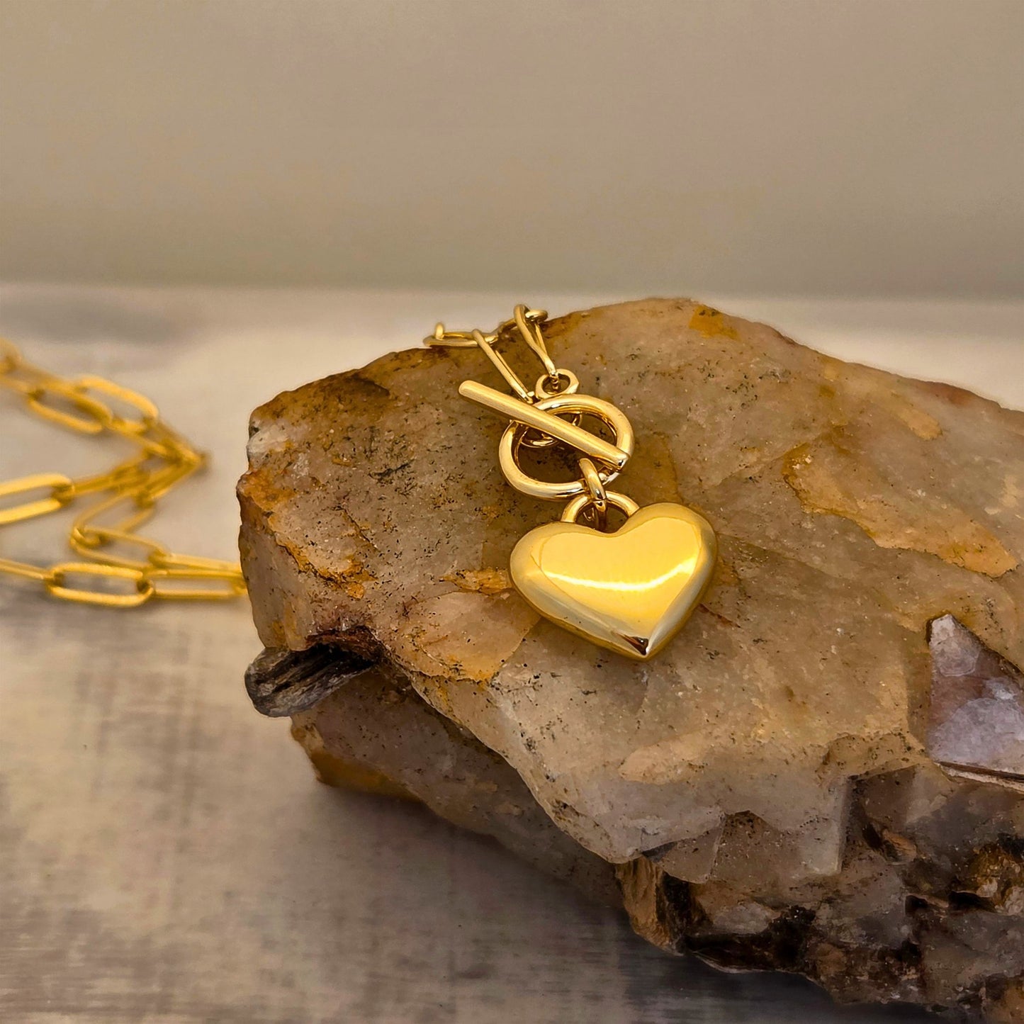 Gold heart-shaped pendant on a gold chain resting on a rock.