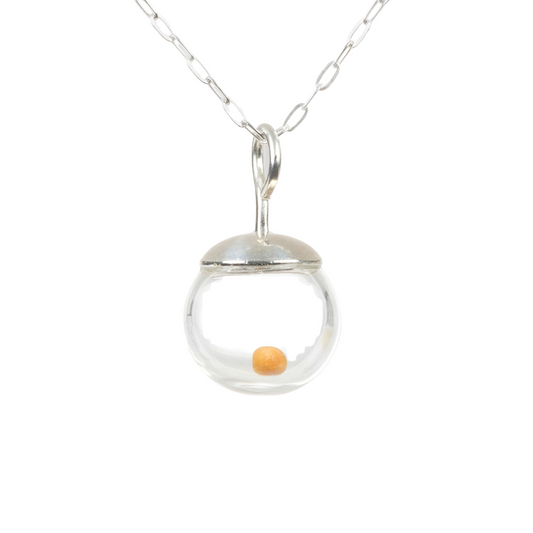 Close-up photo of a delicate 10mm mustard seed necklace (pendant is slightly less than 1/2 inch diameter)  featuring a tiny real mustard seed encased in a clear hand-blown glass globe. The globe is topped with a smooth, solid 925 sterling silver cap and suspended from a fine sterling silver cable chain. The mustard seed floats freely inside the miniature globe, creating a simple yet meaningful design.