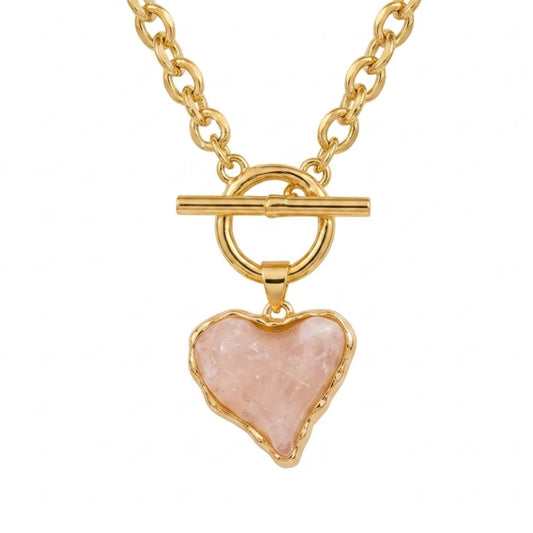 A professional product photo of a gold-plated paperclip chain necklace hanging in a V-formation on a pure white background, featuring a center toggle clasp closure with a dangling, raw-edged pink acrylic heart pendant encased in a gold border.