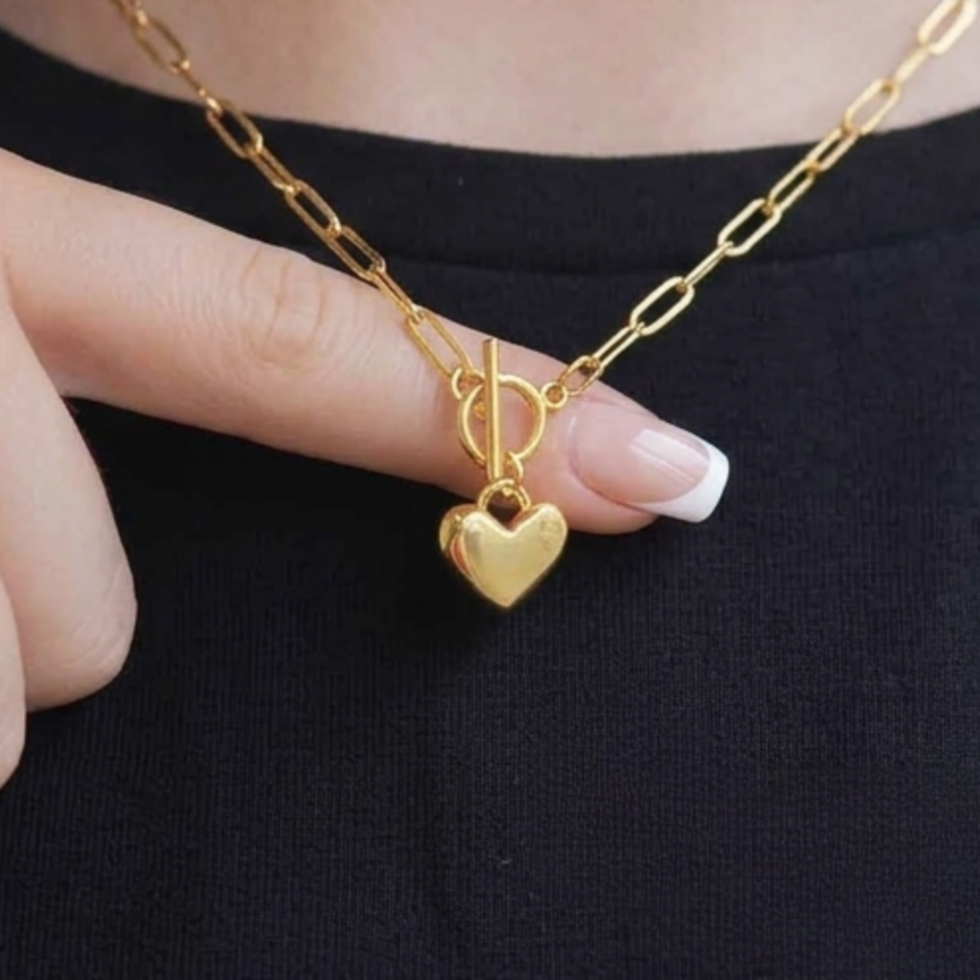 Gold necklace with a heart pendant held by a hand against a black background