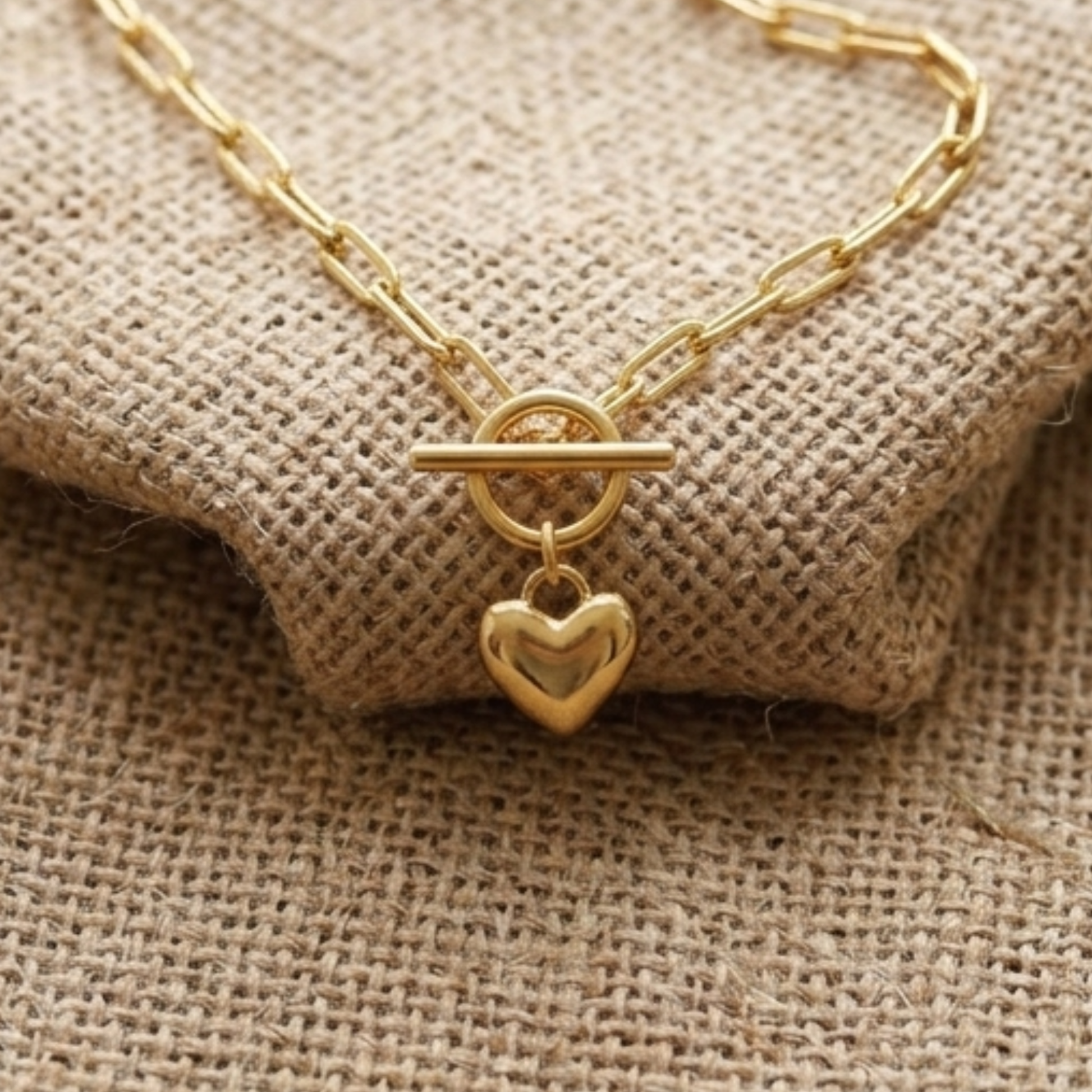 Gold necklace with a heart-shaped clasp on a textured beige fabric background