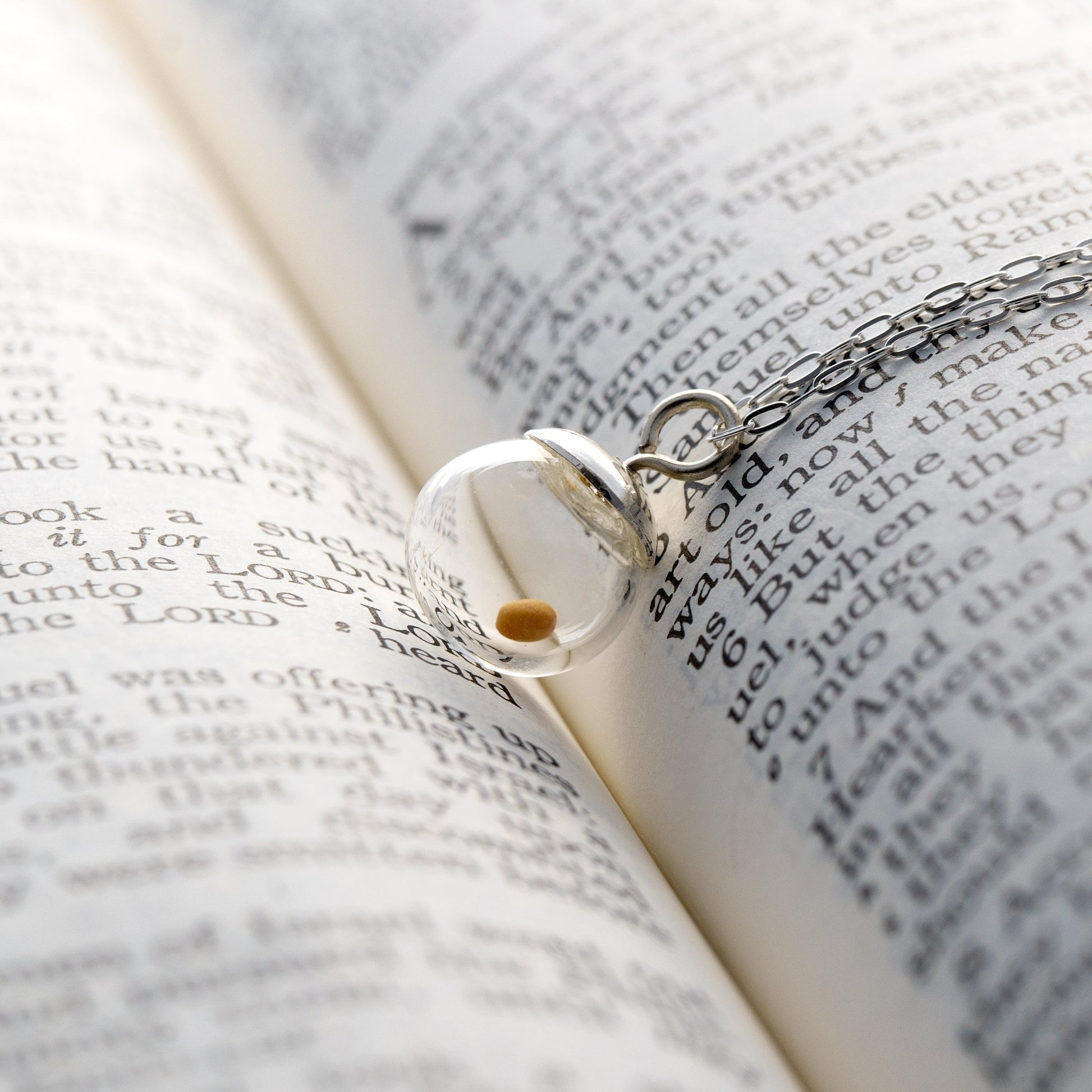 Regular 10mm (slightly less than 1/2 inch diameter) sterling silver mustard seed pendant necklace laying in the crease of an open bible.