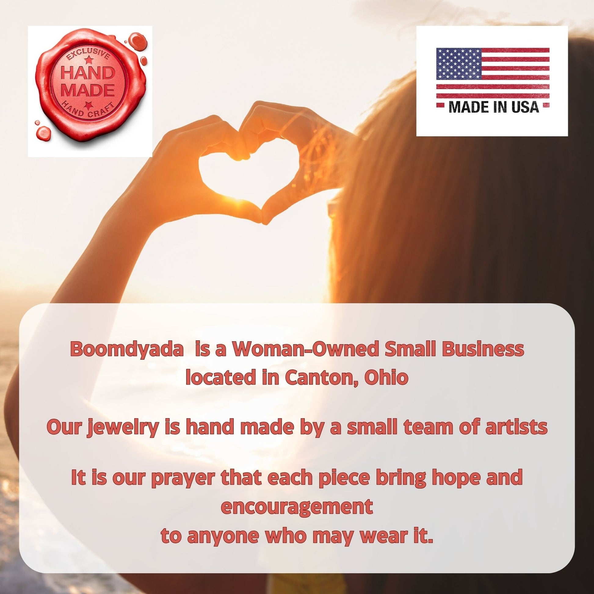 A woman forms a heart shape with her hands in front of a sunlit background. The image features two icons: a red wax seal reading "Exclusive Hand Made Hand Craft" and a U.S. flag labeled "Made in USA." Overlaid text shares that Boomdyada is a woman-owned small business located in Canton, Ohio, where a small team of artists handcrafts jewelry with the hope of bringing encouragement and hope to the wearer.
