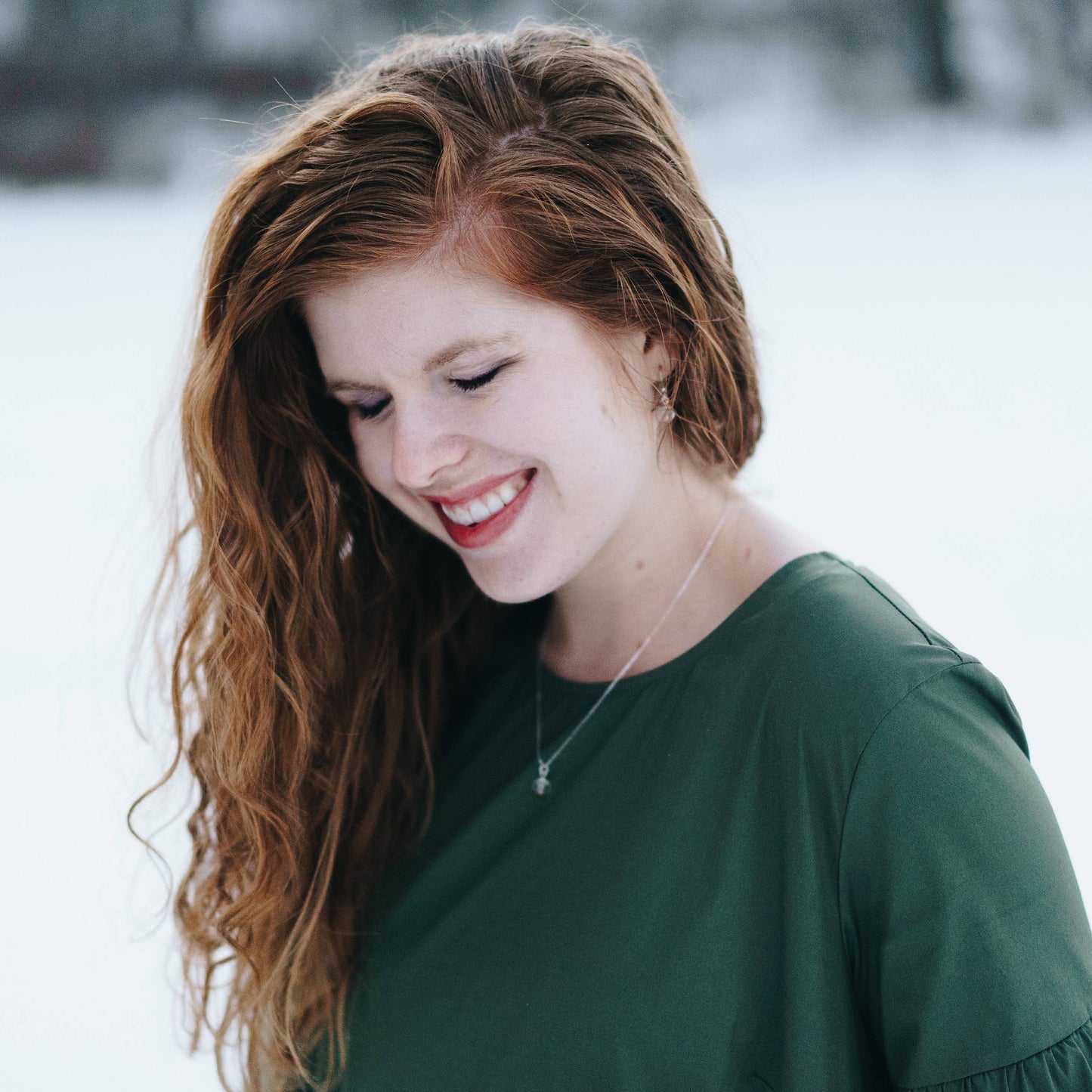 Red headed woman wearing a dark green top wearing the regular 10mm sterling silver mustard seed necklace on a 20 inch long chain and the matching sterling silver mustard seed earrings.